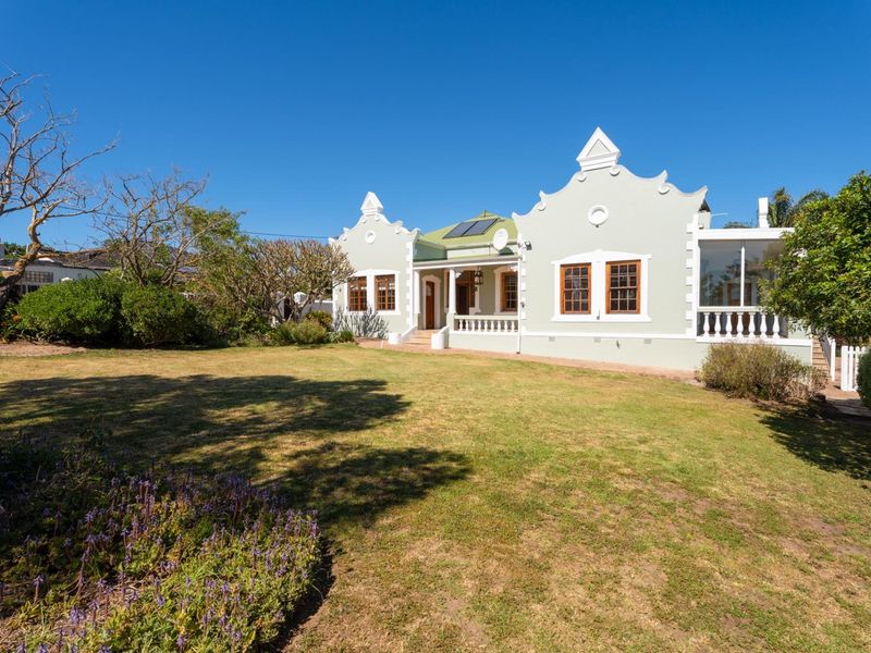 A well-maintained Cape Dutch style home featuring a spacious rear garden, covered patio, and solar water heating panels on the roof.