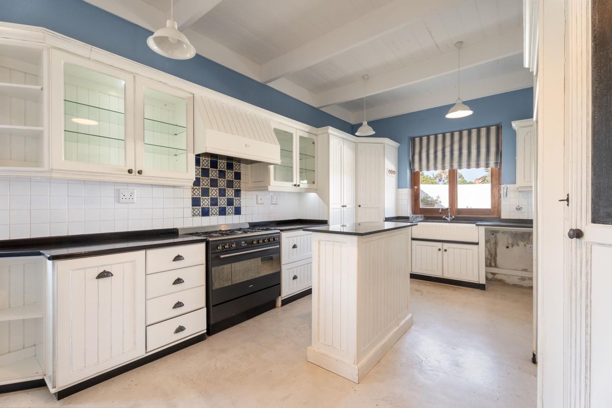 A country-style kitchen featuring white cabinetry, a central island, gas stove, farmhouse sink, and exposed beam ceilings with blue accent walls.