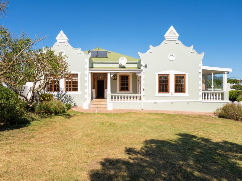 A well-maintained Cape Dutch style home featuring distinctive gables, timber sash windows, a covered veranda, and solar water heating panels set in a garden.
