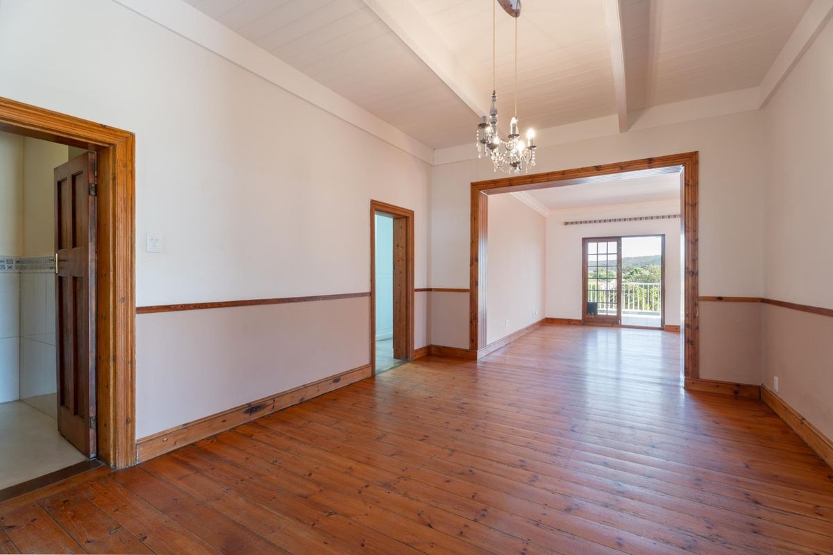 Spacious living area featuring polished timber flooring, exposed beam ceilings, and classic timber trim, leading to an outdoor balcony with scenic views.