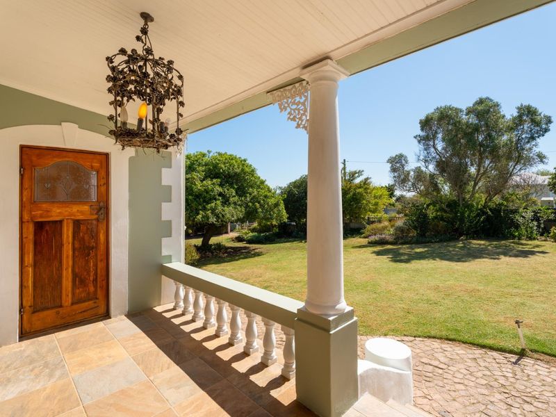 A covered patio featuring stone tile flooring, a decorative wrought iron chandelier, and a classic balustrade overlooking a spacious garden.