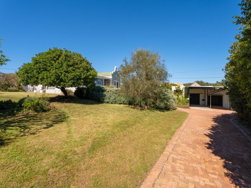 A view of the property's front exterior featuring a brick driveway, carport, and well-maintained garden area leading to the main house.
