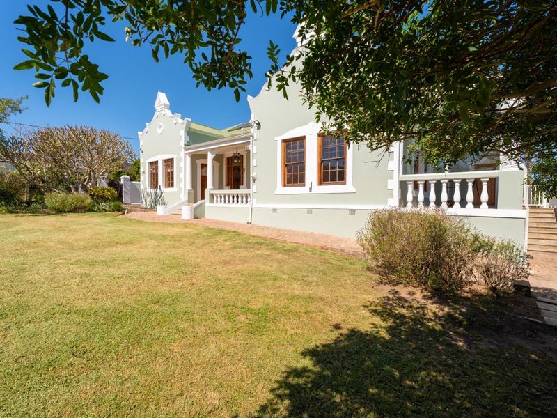 A well-maintained Cape Dutch style home featuring a covered veranda, classic timber sash windows, and a spacious rear garden with brick paved pathways.