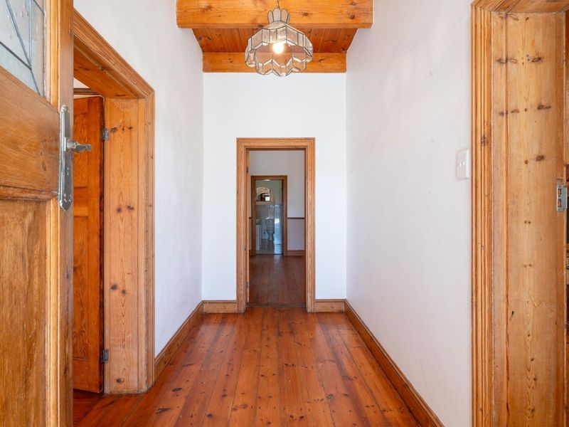 A bright hallway featuring warm timber flooring, exposed wooden ceiling beams, and classic timber door frames leading to adjacent rooms.