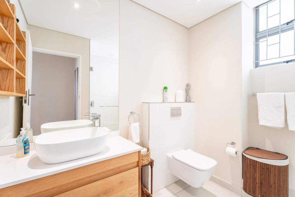 Modern bathroom featuring a wall-mounted toilet with concealed cistern, a wooden vanity with a vessel sink, and built-in shelving.