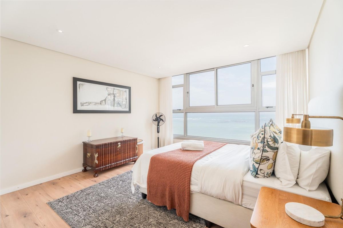 A bright and modern bedroom featuring timber flooring, recessed lighting, and a large window offering expansive ocean views.