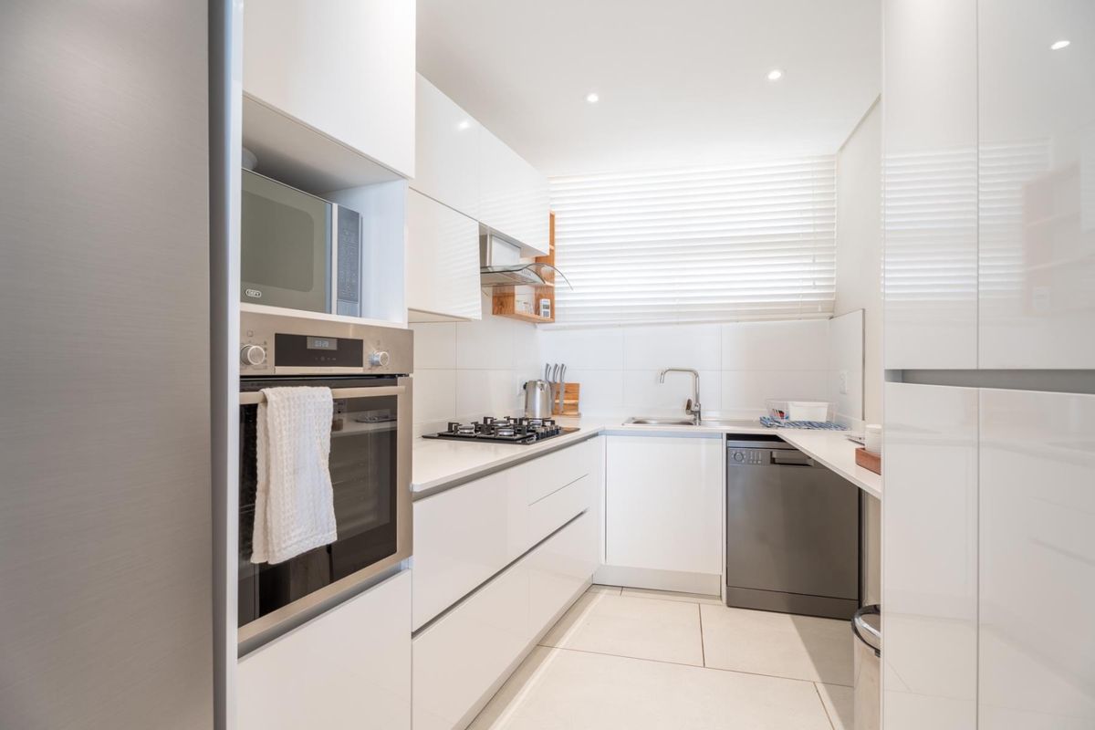Modern, well-maintained kitchen featuring sleek white cabinetry, built-in oven, gas hob, integrated dishwasher, and clean tiled finishes.