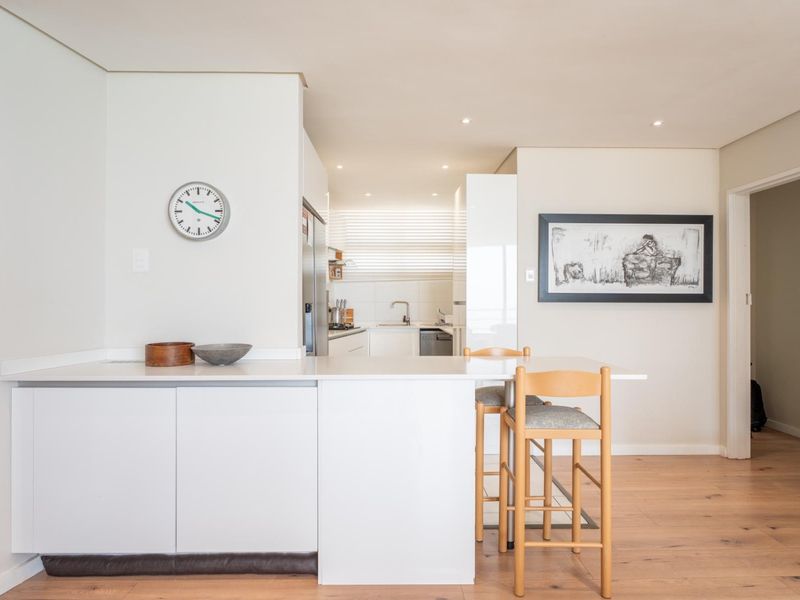 A bright open-plan living and kitchen area featuring modern white cabinetry, a functional kitchen island, and warm timber flooring throughout.