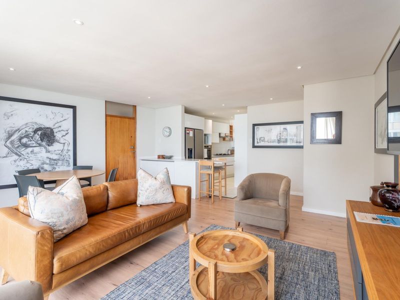 An open-plan living and dining area featuring light laminate flooring, recessed lighting, and a modern kitchen with a functional island and built-in appliances.
