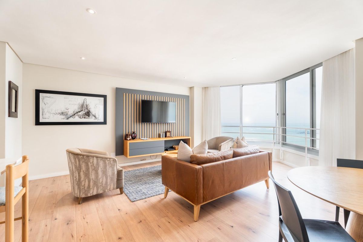 Bright and modern living area featuring timber flooring, a custom slatted media wall, and expansive floor-to-ceiling windows with ocean views.