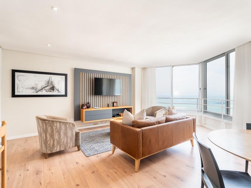 Bright and modern living area featuring timber flooring, a custom slatted media wall, and expansive floor-to-ceiling windows with ocean views.