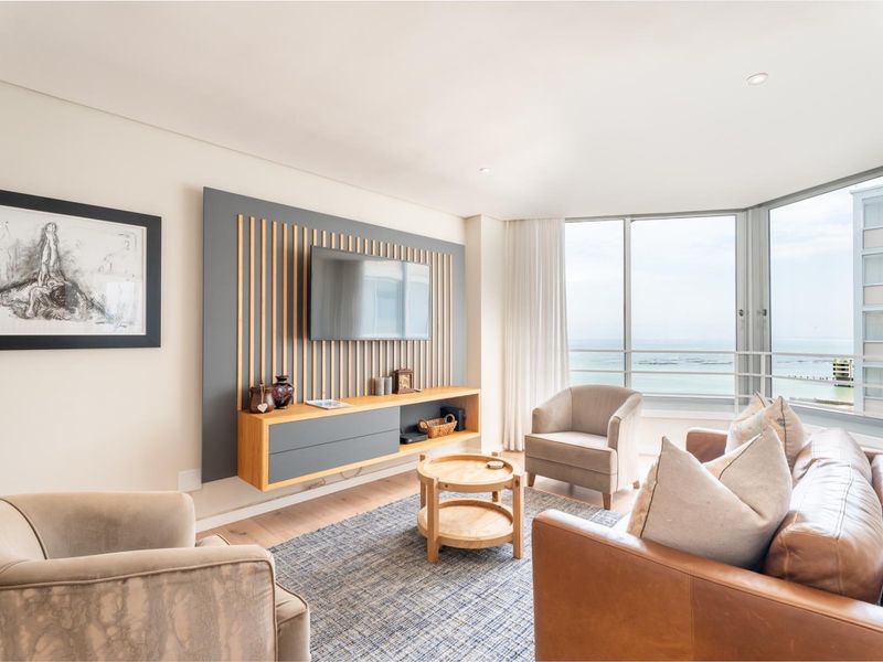 Modern living room featuring a custom built-in media console with slatted timber detailing, recessed lighting, and expansive floor-to-ceiling windows with ocean views.