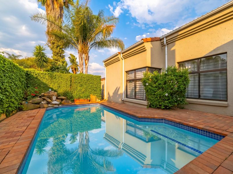 A well-maintained swimming pool area featuring brick paving, a rock water feature, and established privacy hedging against the rear building elevation.