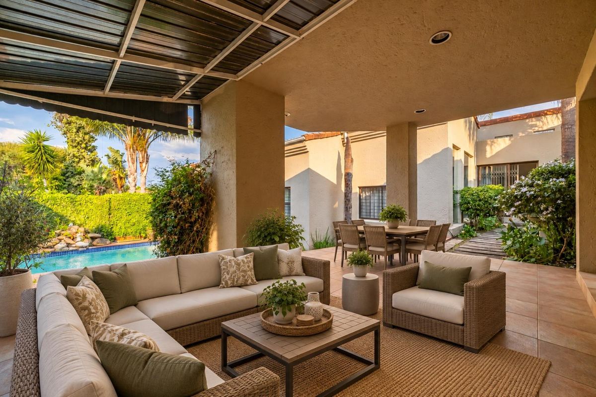 Spacious covered patio area featuring tiled flooring and recessed lighting, overlooking a private swimming pool and landscaped garden.