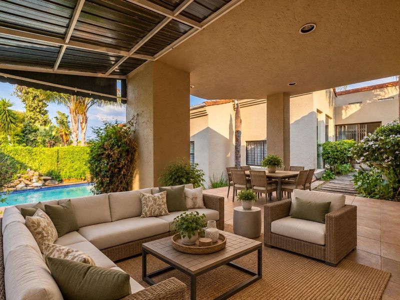 Spacious covered patio area featuring tiled flooring and recessed lighting, overlooking a private swimming pool and landscaped garden.
