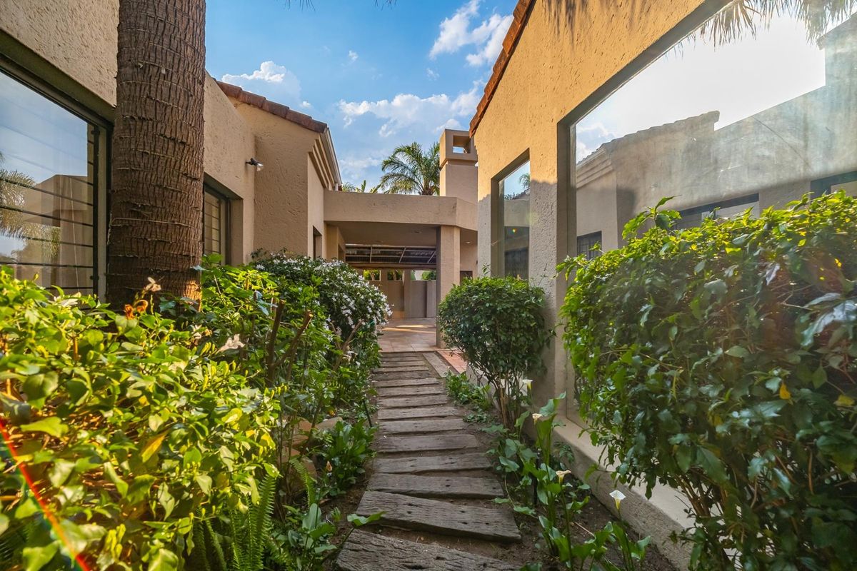 A landscaped rear garden pathway leading between two wings of the house, featuring a covered walkway and an outdoor fireplace chimney.
