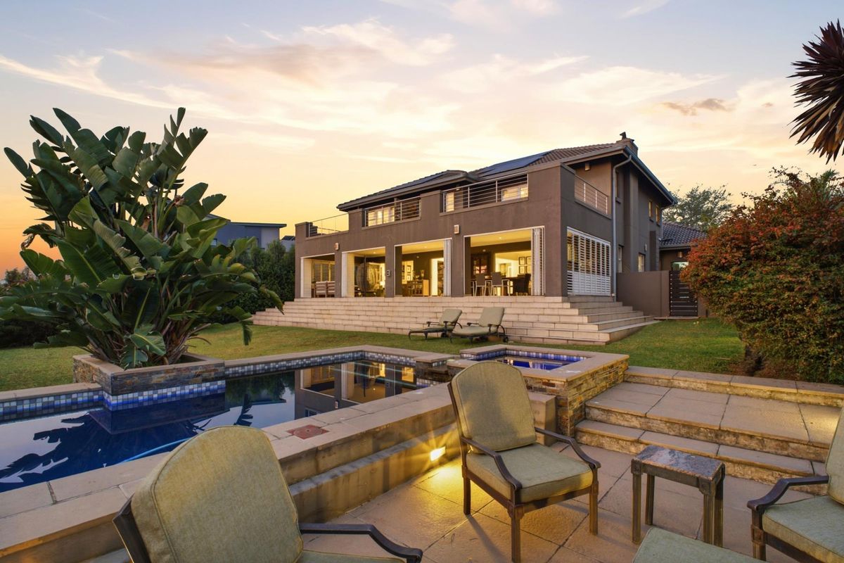 A beautifully presented rear exterior view featuring a modern swimming pool, raised stone patio, and a spacious two-story home with large sliding doors.