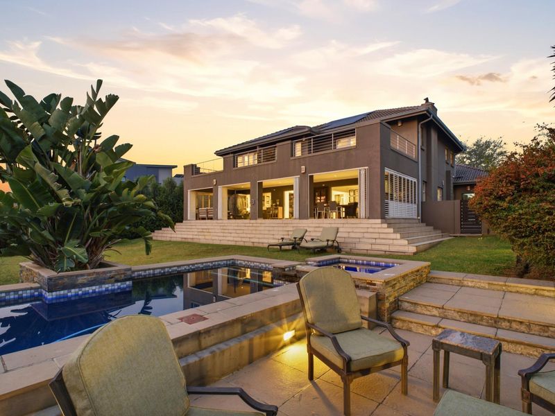 A beautifully presented rear exterior view featuring a modern swimming pool, raised stone patio, and a spacious two-story home with large sliding doors.