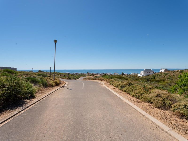 A view looking down a paved residential street towards the ocean, showcasing the coastal landscape and surrounding neighborhood.