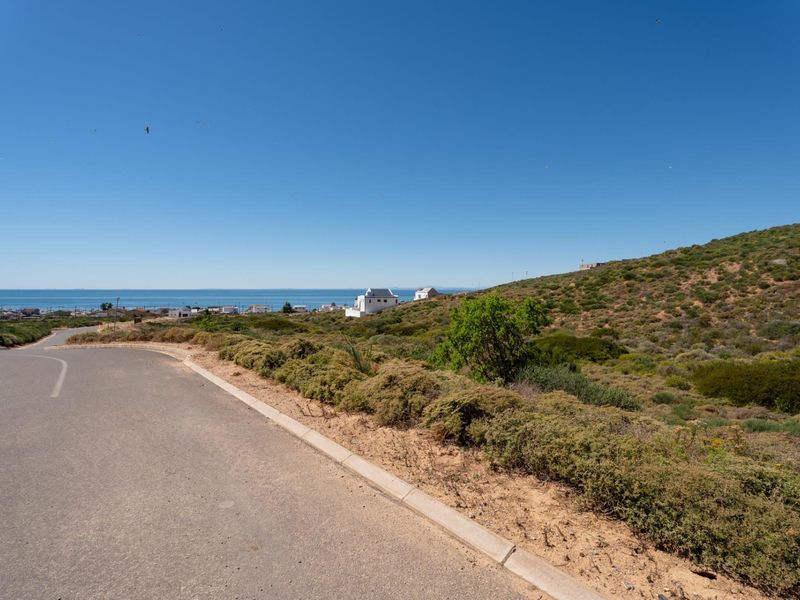 A view of the paved street and curb bordering the vacant residential land, featuring coastal and hillside views in the distance.