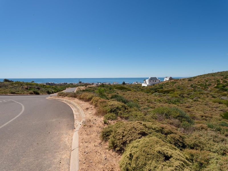 A view of the asphalt street and curb bordering the vacant residential land, featuring coastal landscape and distant ocean views.