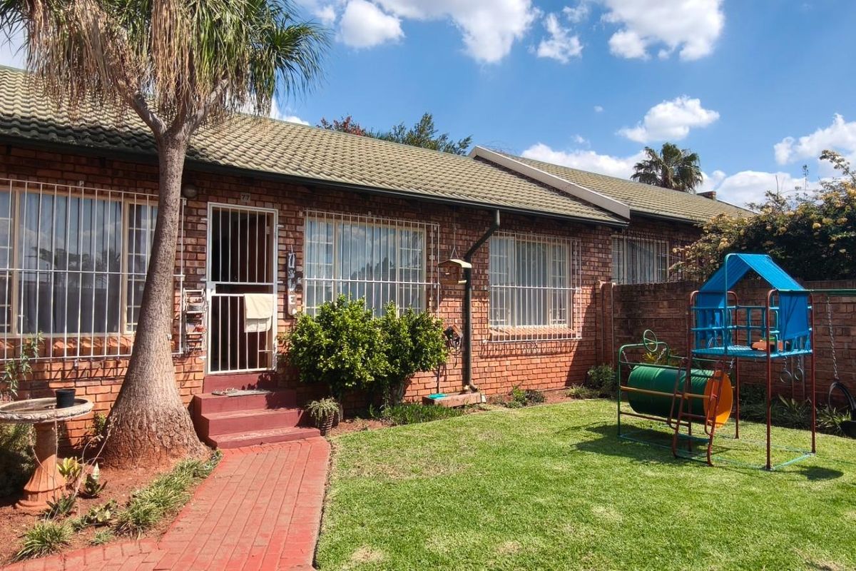 Rear view of the townhouse featuring a brick facade, tiled roof, security bars on windows, and a private garden area with a brick pathway.