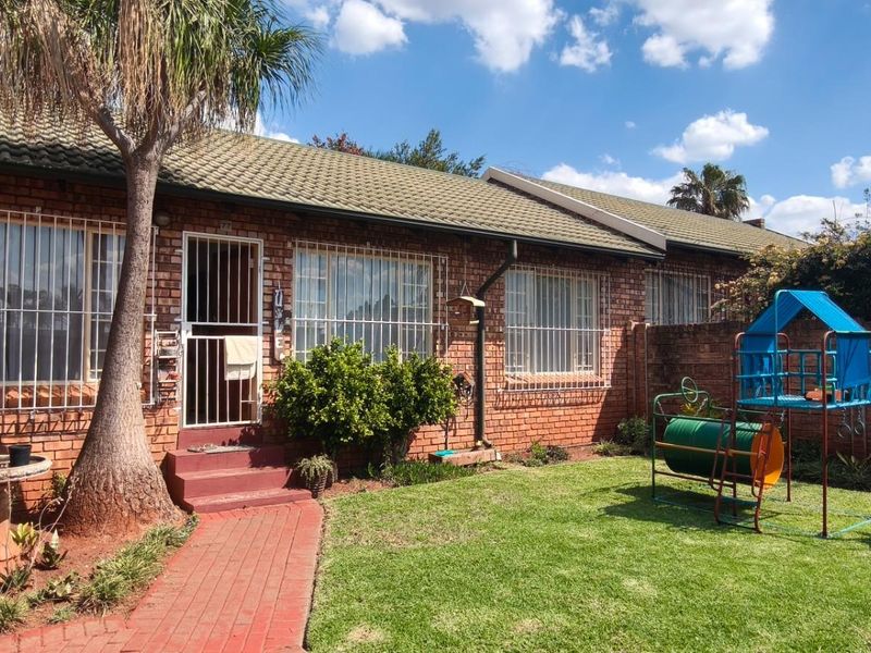 Rear view of the townhouse featuring a brick facade, tiled roof, security bars on windows, and a private garden area with a brick pathway.