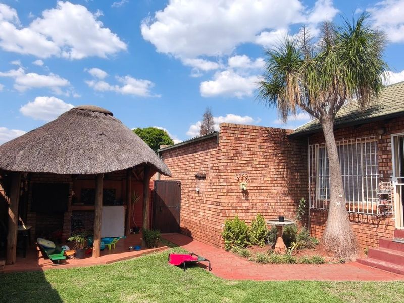 Rear garden area featuring a traditional thatch lapa, brick boundary walls with electric fencing, and a paved patio area adjacent to the townhouse.