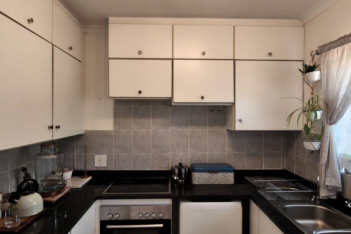 A functional kitchen featuring white cabinetry, black granite countertops, a tiled backsplash, and integrated cooking appliances.