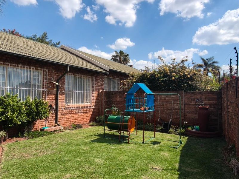 A private rear garden featuring a lawn, paved walkway, and face brick townhouse exterior with security features and perimeter electric fencing.