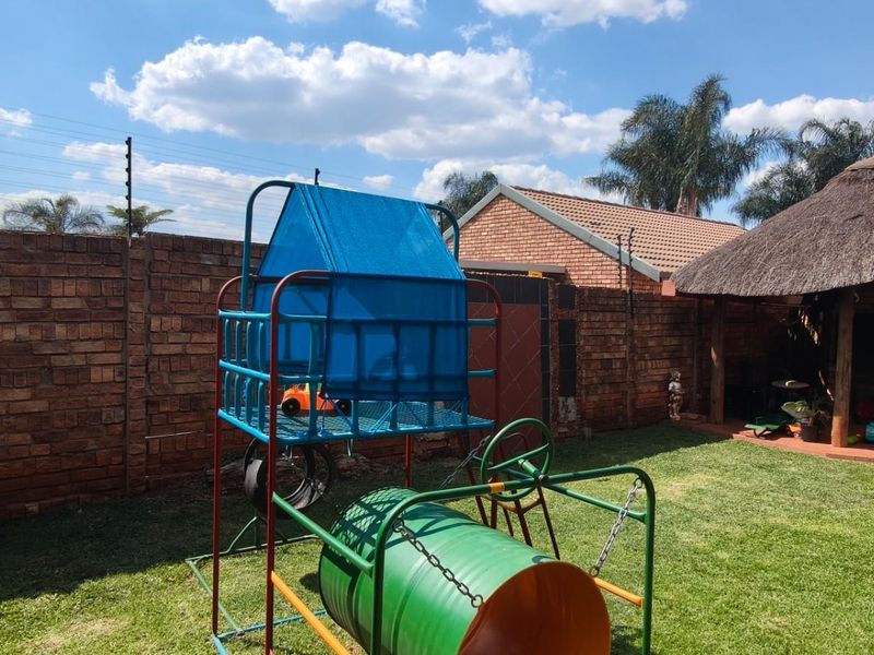 A private rear garden featuring a brick boundary wall with electric fencing and a traditional thatched lapa, providing a functional outdoor entertainment space.