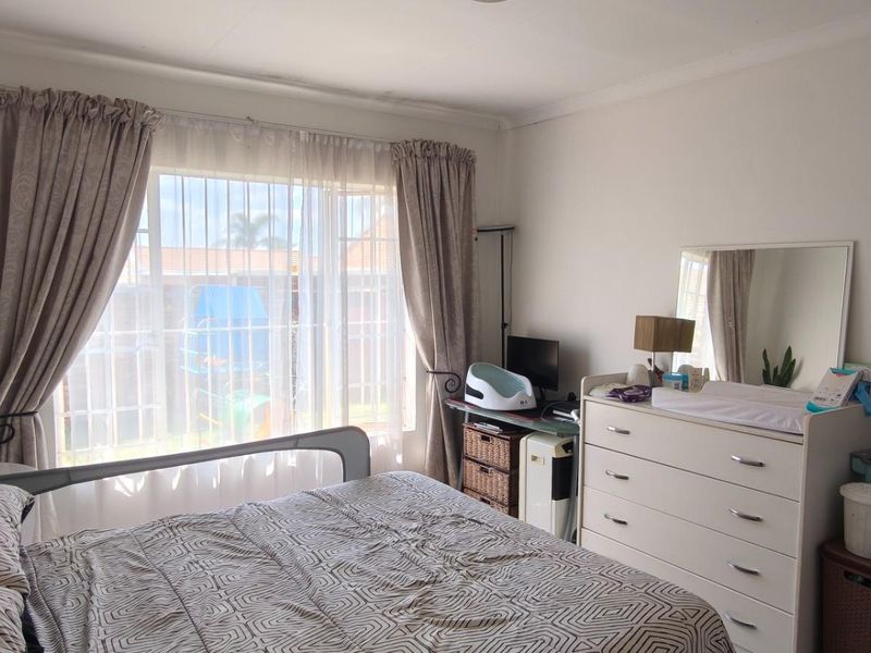 A functional bedroom featuring a large window with security bars and neutral wall finishes, offering a comfortable and well-lit living space.