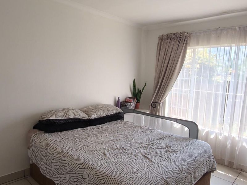 A bright bedroom featuring tiled flooring and a large window with curtain rails, providing natural light and a view of the exterior.