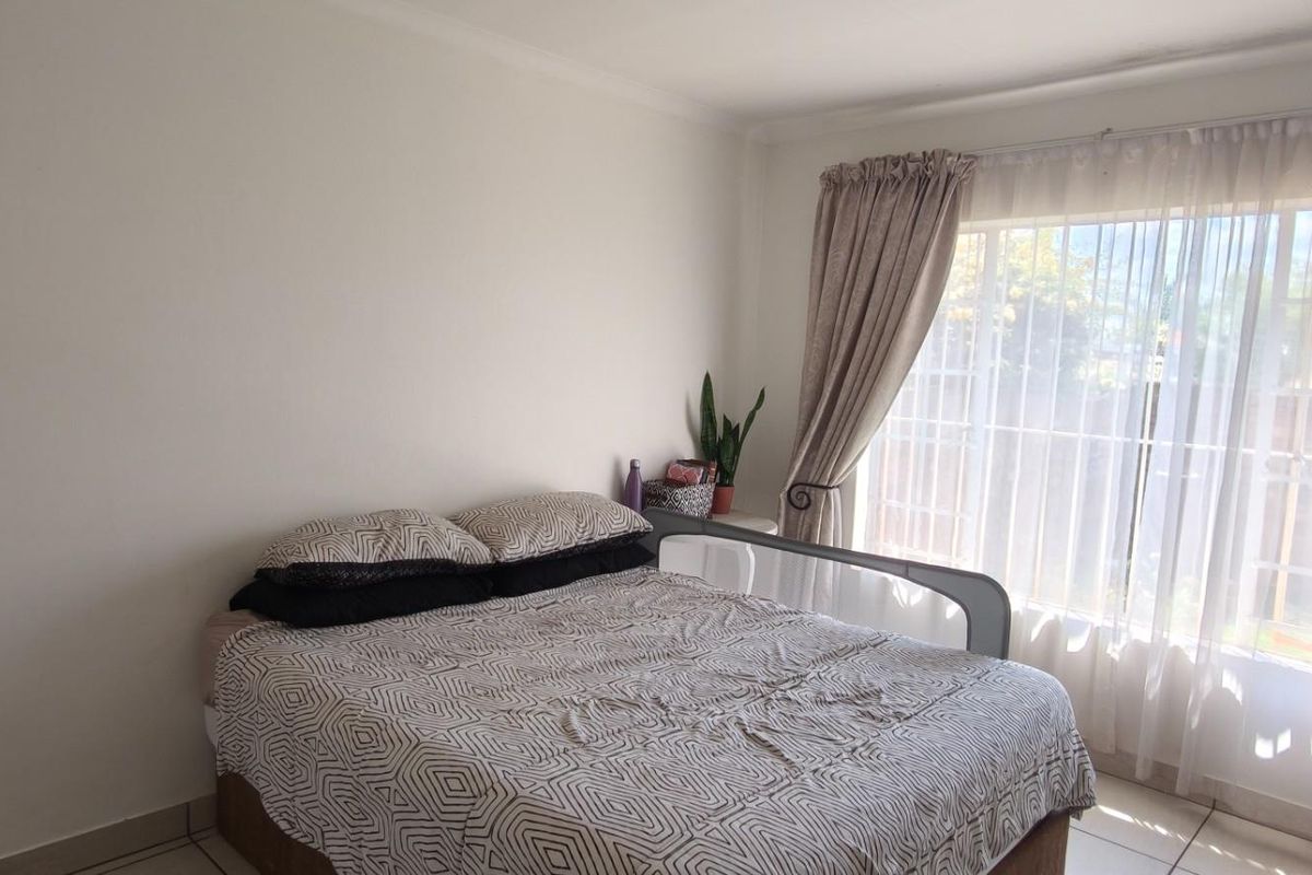 A bright bedroom featuring tiled flooring and a large window with curtain rails, providing natural light and a view of the exterior.