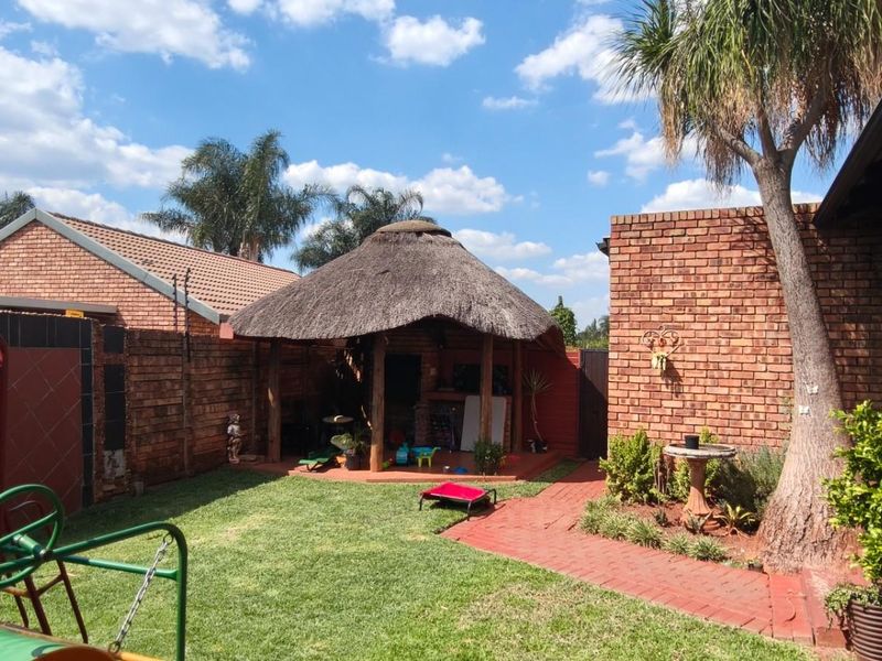 Rear garden area featuring a traditional thatched lapa, brick paving, and established lawn, providing a functional outdoor entertainment space.