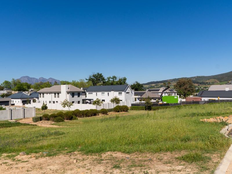 A vacant residential plot of land situated in a developed estate, featuring surrounding residential homes and mountain views.