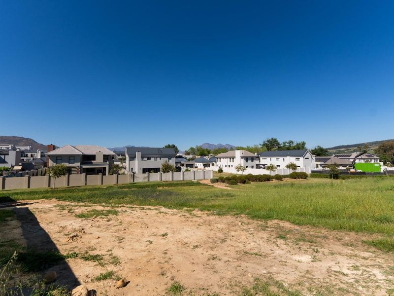 A view of a vacant residential plot in a developed estate, featuring surrounding homes and clear boundary walls.