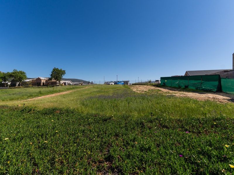 A vacant residential plot of land featuring natural ground cover and perimeter fencing, situated in a developing neighborhood.