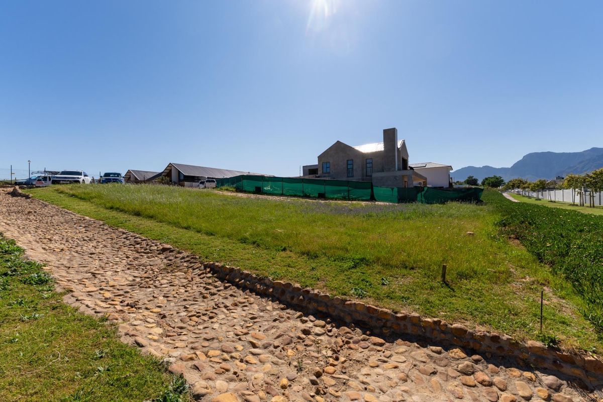 A vacant residential plot featuring a stone pathway and a partially constructed building enclosed by green construction fencing.