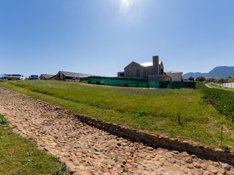 A vacant residential plot featuring a stone pathway and a partially constructed building enclosed by green construction fencing.