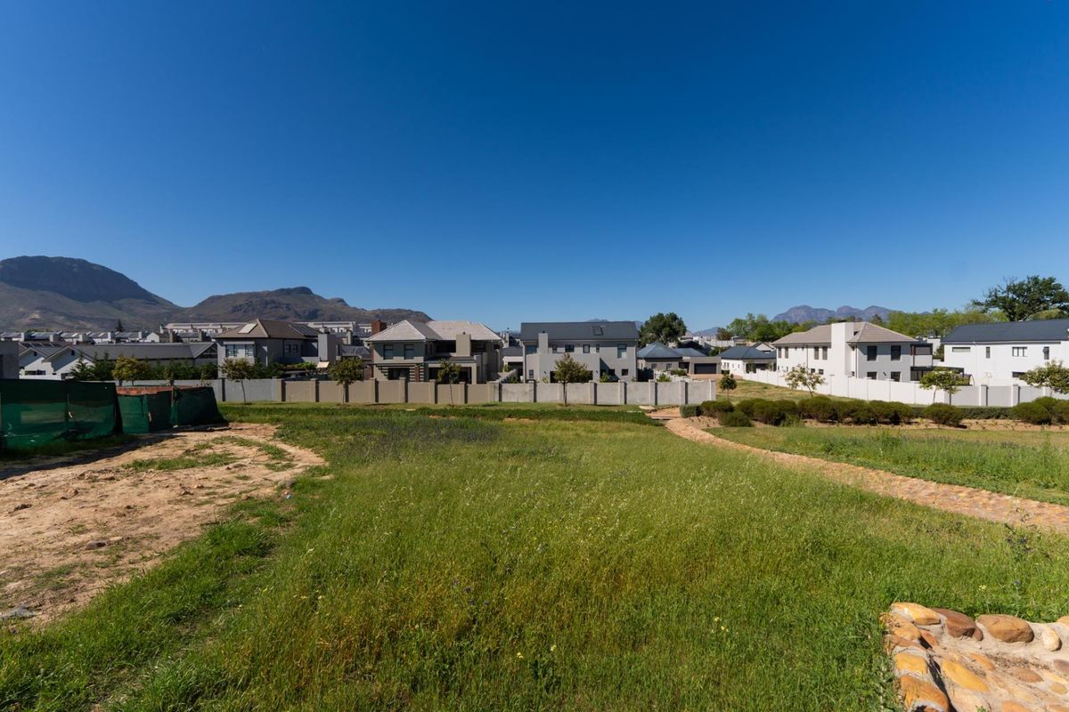 A vacant residential plot featuring open grass areas and a perimeter wall, offering views of the surrounding neighborhood and distant mountains.