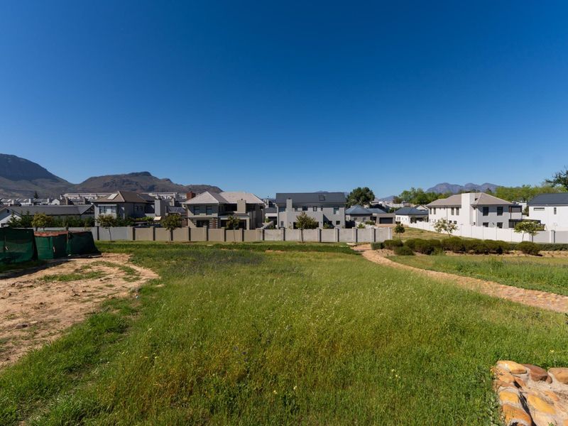 A vacant residential plot featuring open grass areas and a perimeter wall, offering views of the surrounding neighborhood and distant mountains.