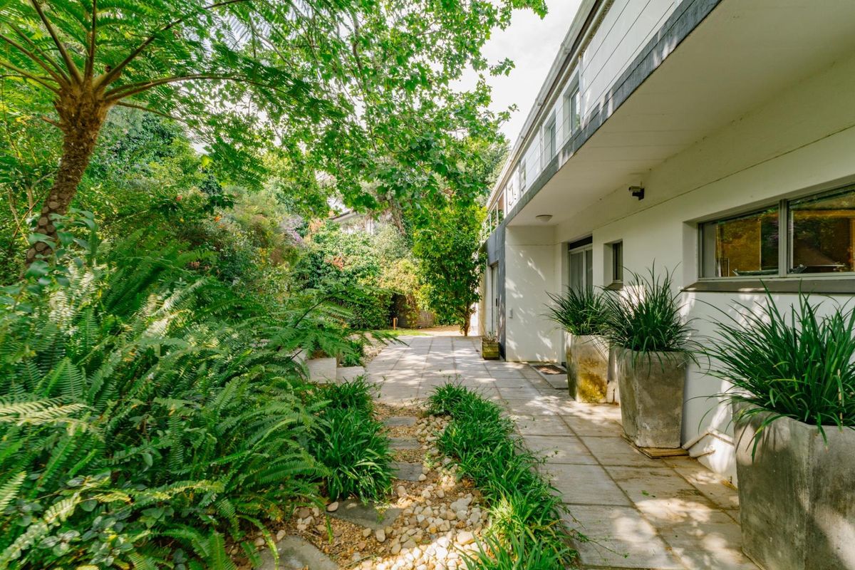 A well-maintained rear garden area featuring a paved walkway, lush greenery, and direct access to the home through sliding glass doors.