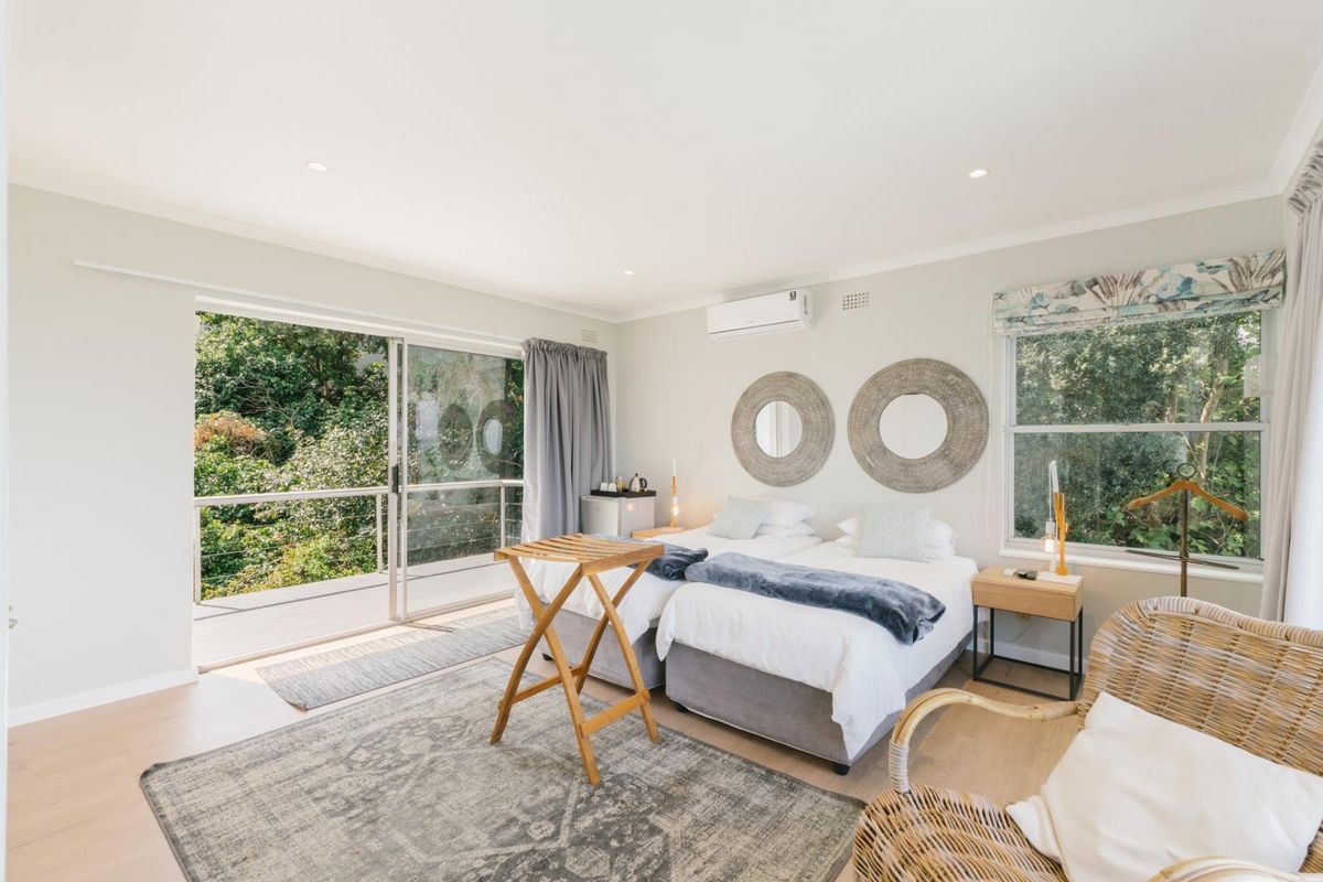 A bright and airy bedroom featuring timber-look flooring, a split-system air conditioner, and large sliding glass doors that open onto an outdoor balcony.