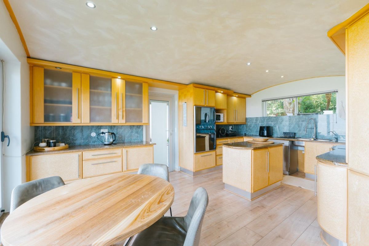Spacious kitchen featuring light wood cabinetry, stone countertops, a central island, and integrated appliances, offering a functional layout with ample storage space.