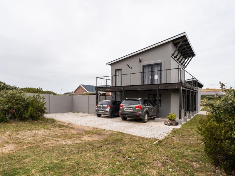 Modern two-story house featuring a mono-pitch roof, a spacious raised timber balcony, and a gravel driveway with perimeter walling.