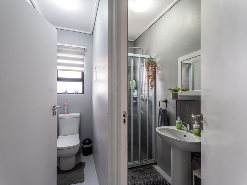 A compact, functional bathroom featuring a pedestal basin, a separate shower enclosure, and a toilet, finished with neutral wall tones.