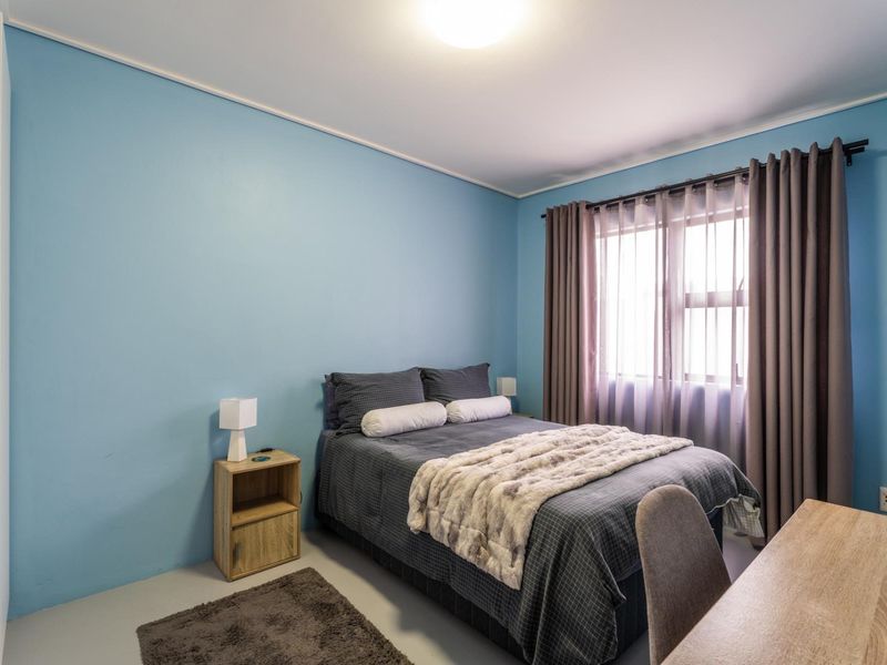 A bedroom featuring blue painted walls, a window with curtains, and standard electrical fixtures.