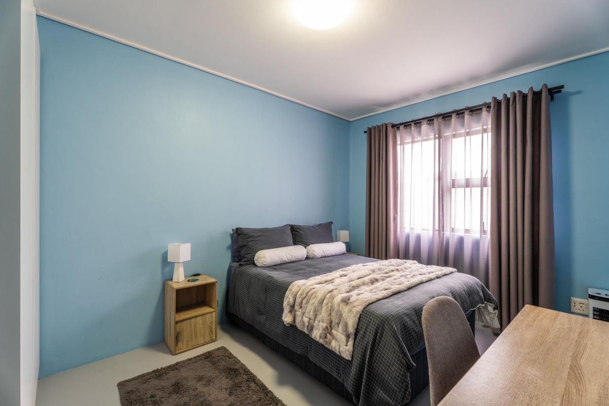 A bedroom featuring blue painted walls, a window with curtains, and standard electrical fixtures.