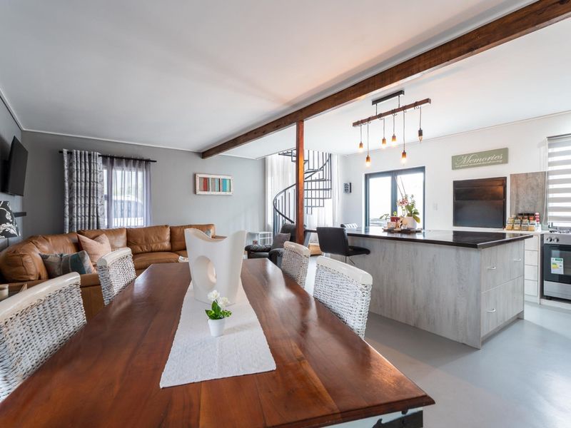 Spacious open-plan living, dining, and kitchen area featuring exposed timber beams, a modern kitchen island, and a striking spiral staircase.